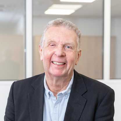 A head and shoulders photograph of BWBF Vice Chair Gerry Thorn, taken in 2024. Gerry is standing in front of a desk smiling. He is wearing a dark suit jacket and pale blue shirt.