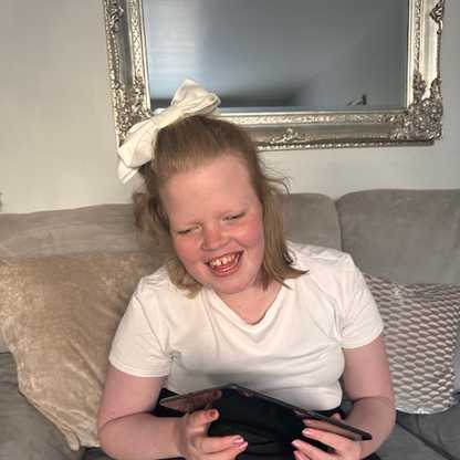A photograph of Madison smiling broadly as she holds an iPad in her arms. She has a bow in her hair.