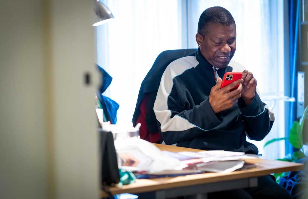 A man smiles as he operates a red mobile phone in his hands