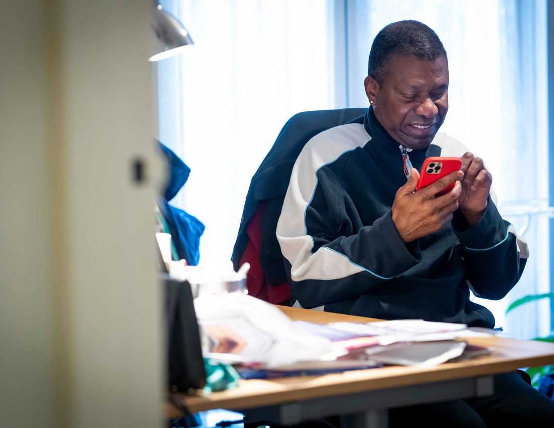 A man smiles as he operates a red mobile phone in his hands