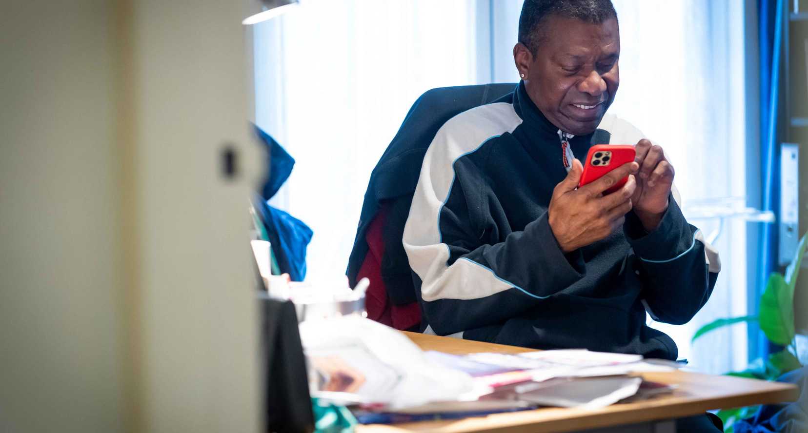 A man smiles as he operates a red mobile phone in his hands